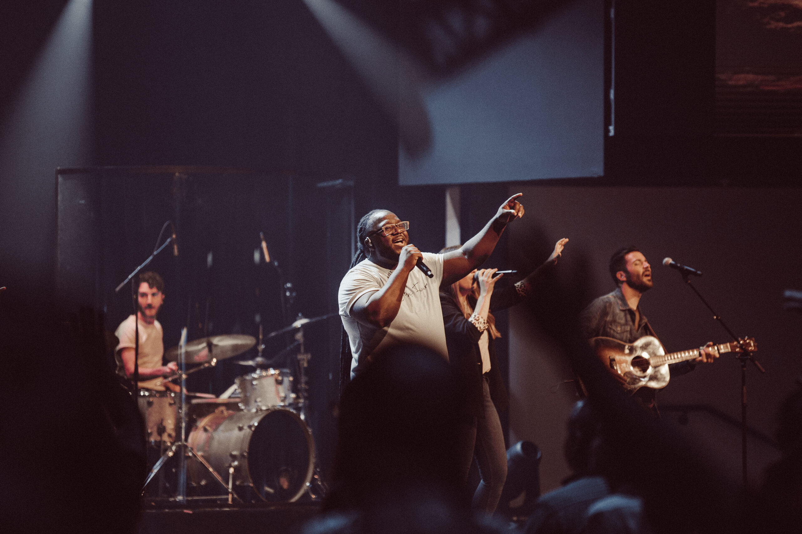 Marcel Joseph & The Houze Band lead in worship from a stage in a dark room.